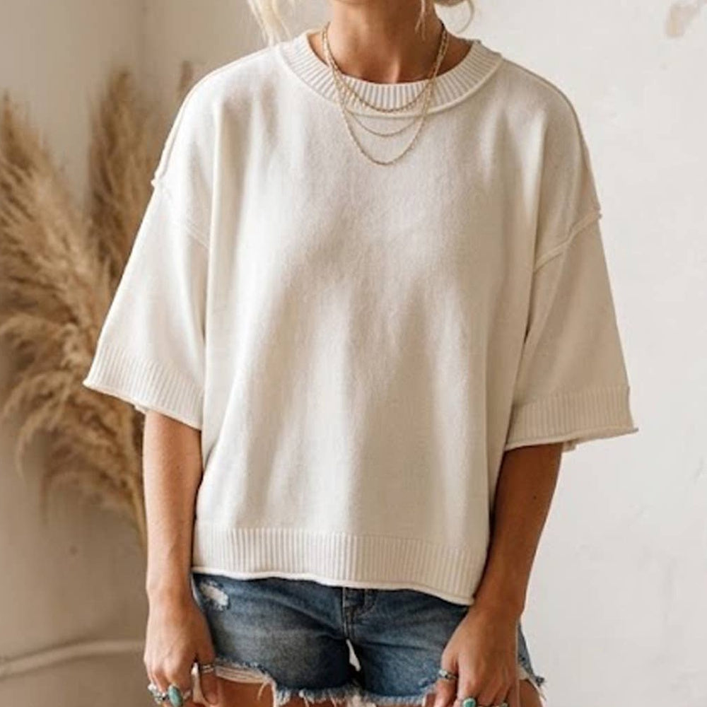 Woman wearing a white, lightweight, oversized short-sleeve knit sweater top paired with denim shorts.