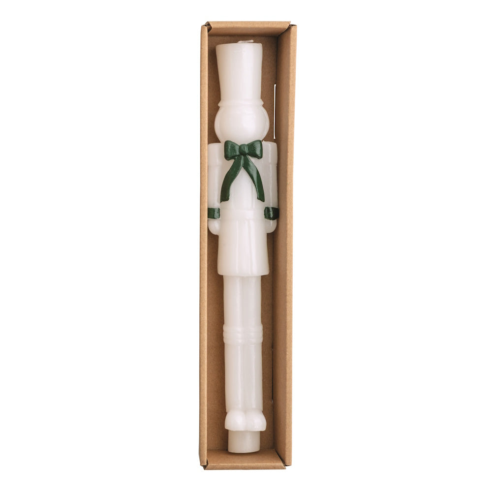 White nutcracker wax taper candle with green accents in a cardboard box, viewed from above.
