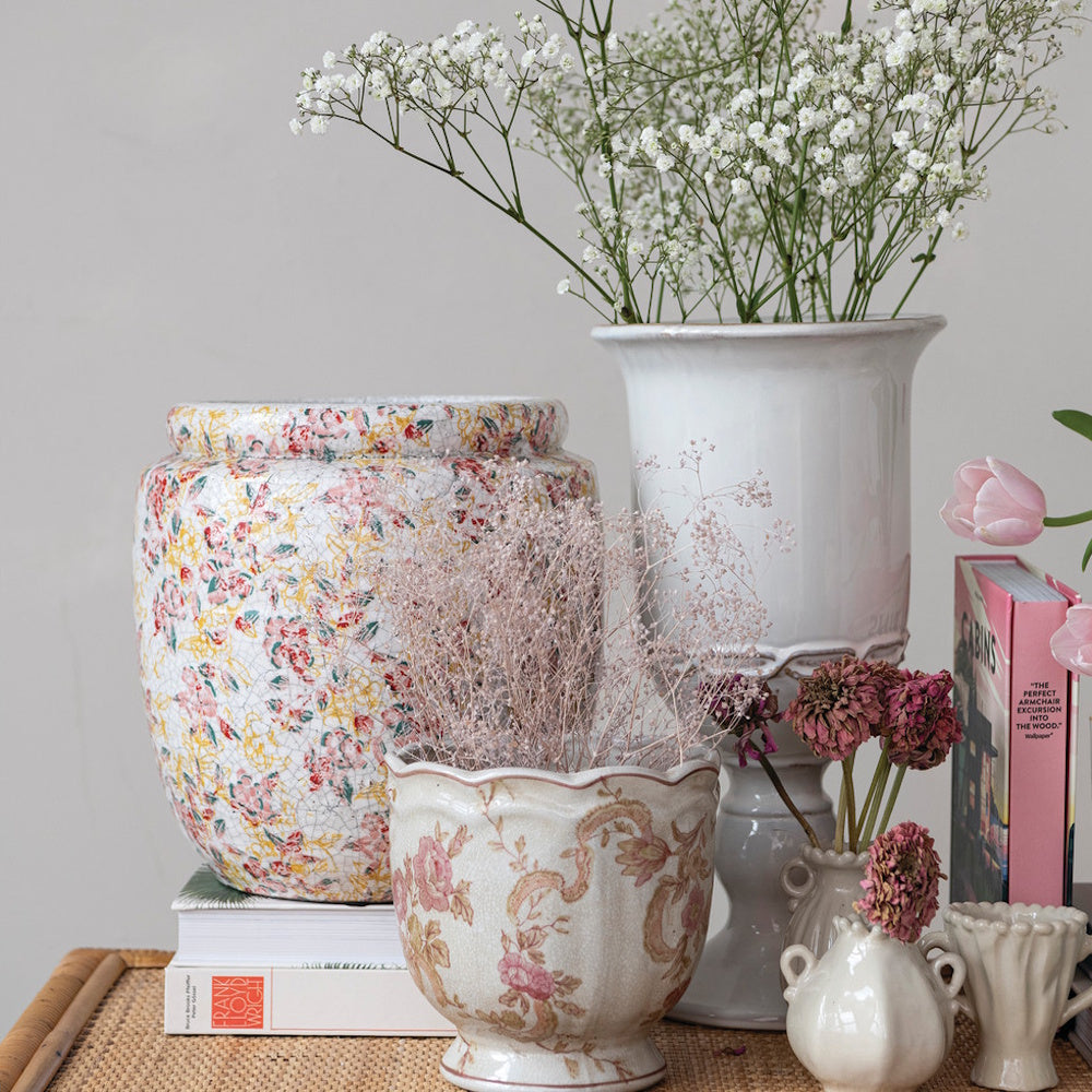 White stoneware urn with baby's breath among floral patterned decorative vases.