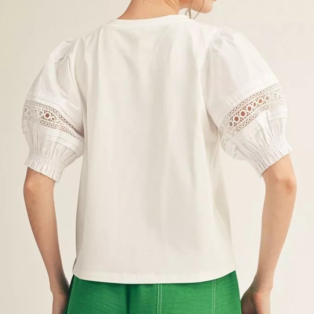 Back view of a woman wearing a white top with lace-detailed puff sleeves and green pants.