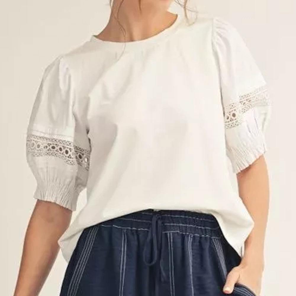 A woman wearing a white blouse with lace-detailed puff sleeves and blue striped pants.