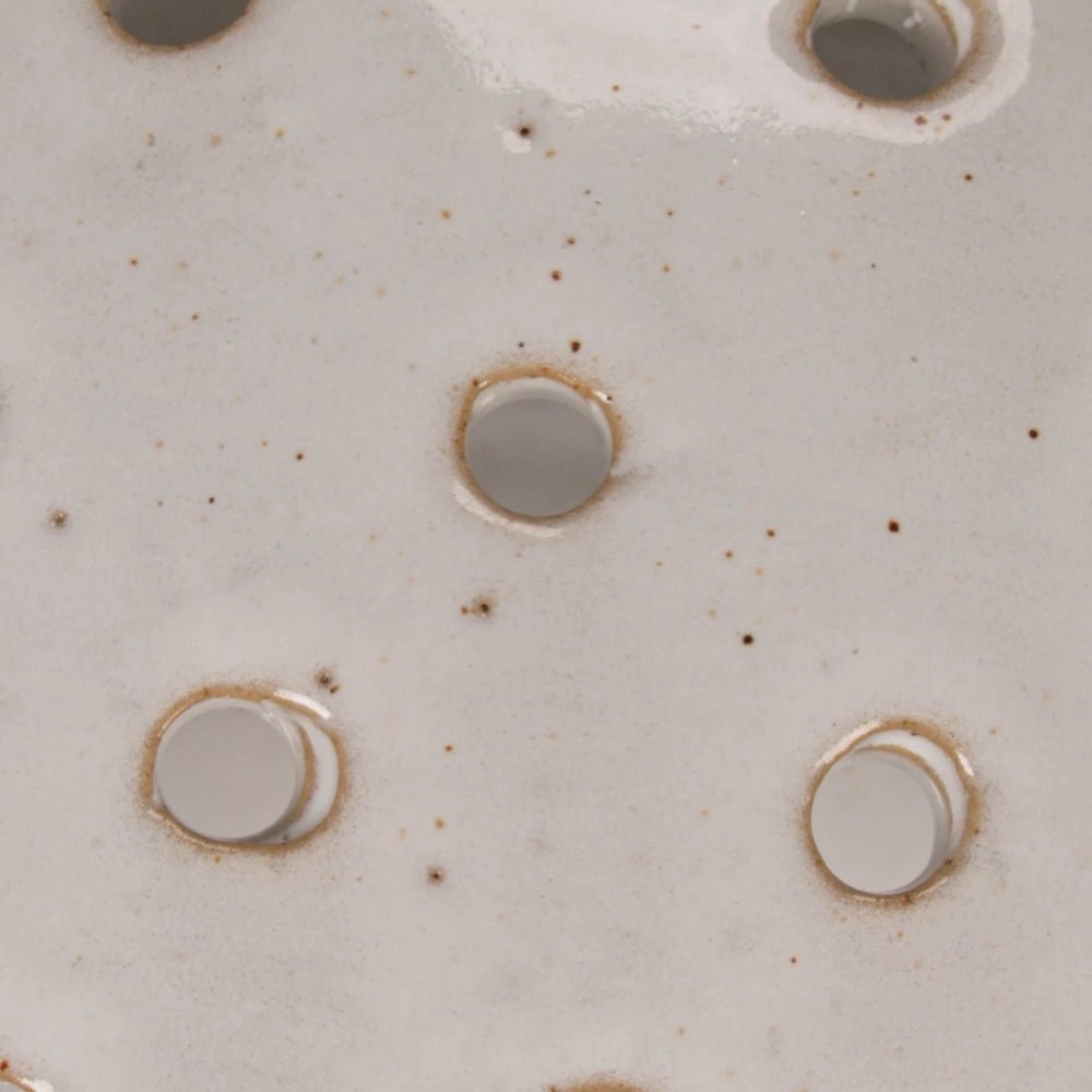 Close-up of white speckled stoneware strainer bowl with circular drainage holes and a glazed finish.