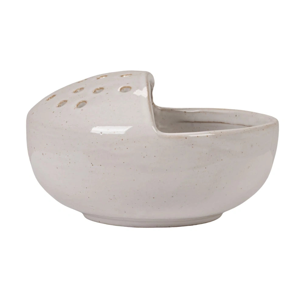 White stoneware strainer bowl with speckled glaze and drainage holes on a raised side on a white background.