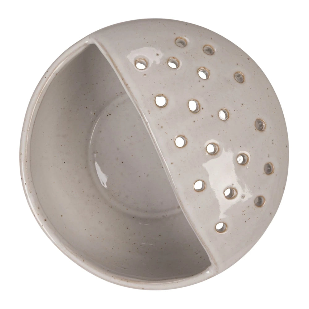 Speckled white stoneware strainer bowl with a built-in drainage side and small circular holes for rinsing food.