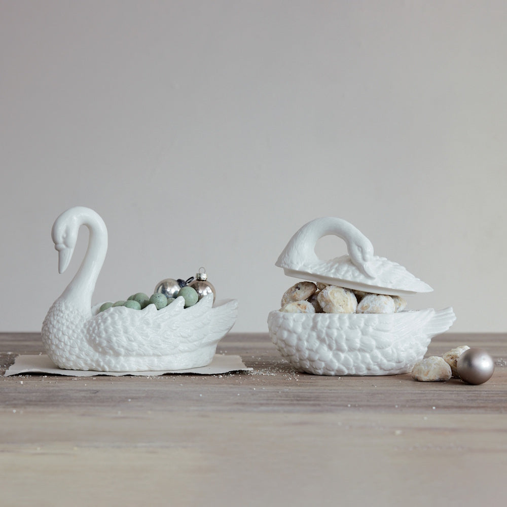 Two white ceramic swan decorative dishes, one filled with mini ornaments and one holding cookies.