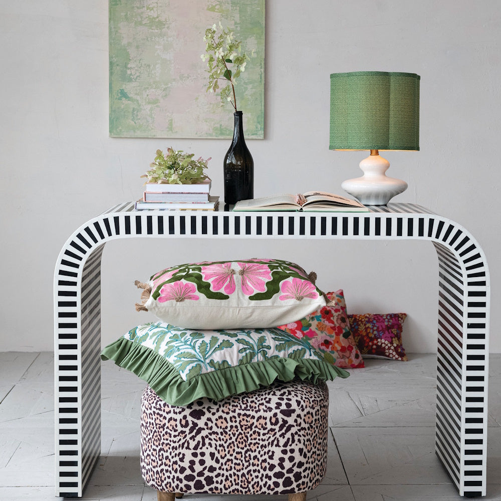 White stoneware table lamp with a green fabric shade on a modern striped console table.