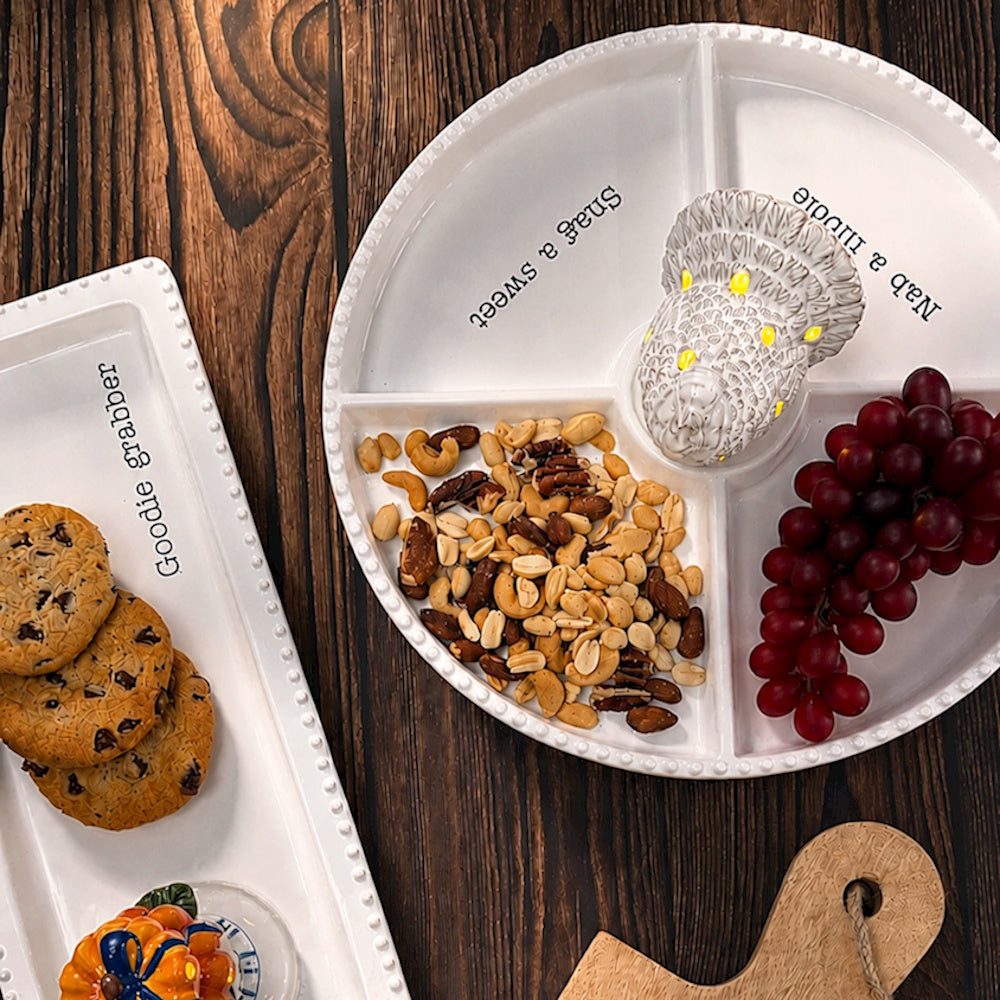White divided ceramic serving tray with turkey center, nuts, grapes, and cookies on wooden table.