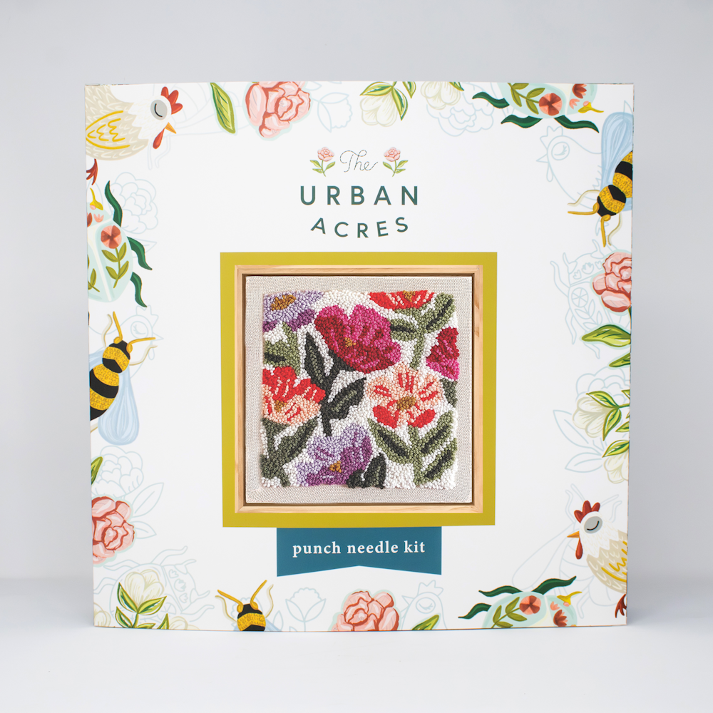 The Urban Acres punch needle kit packaging features a colorful square wildflower design surrounded by floral and bee motifs.