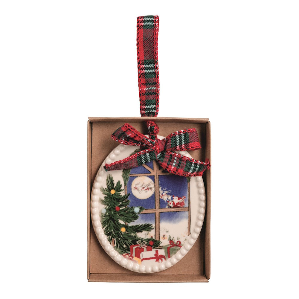Oval ceramic ornament showing a window scene of Santa flying, with plaid ribbon bow and hanging loop.
