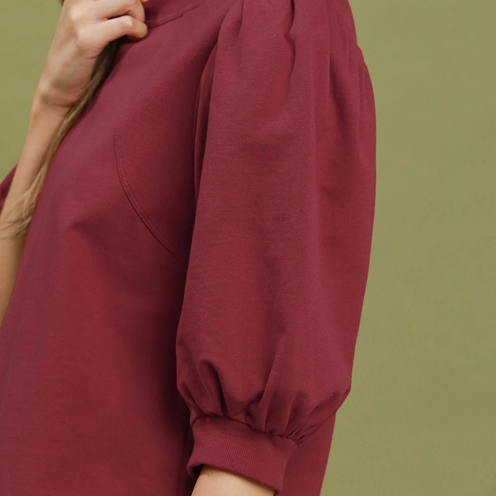 Close-up of a wine red pullover sweatshirt top with voluminous puff sleeves and ribbed cuffs.