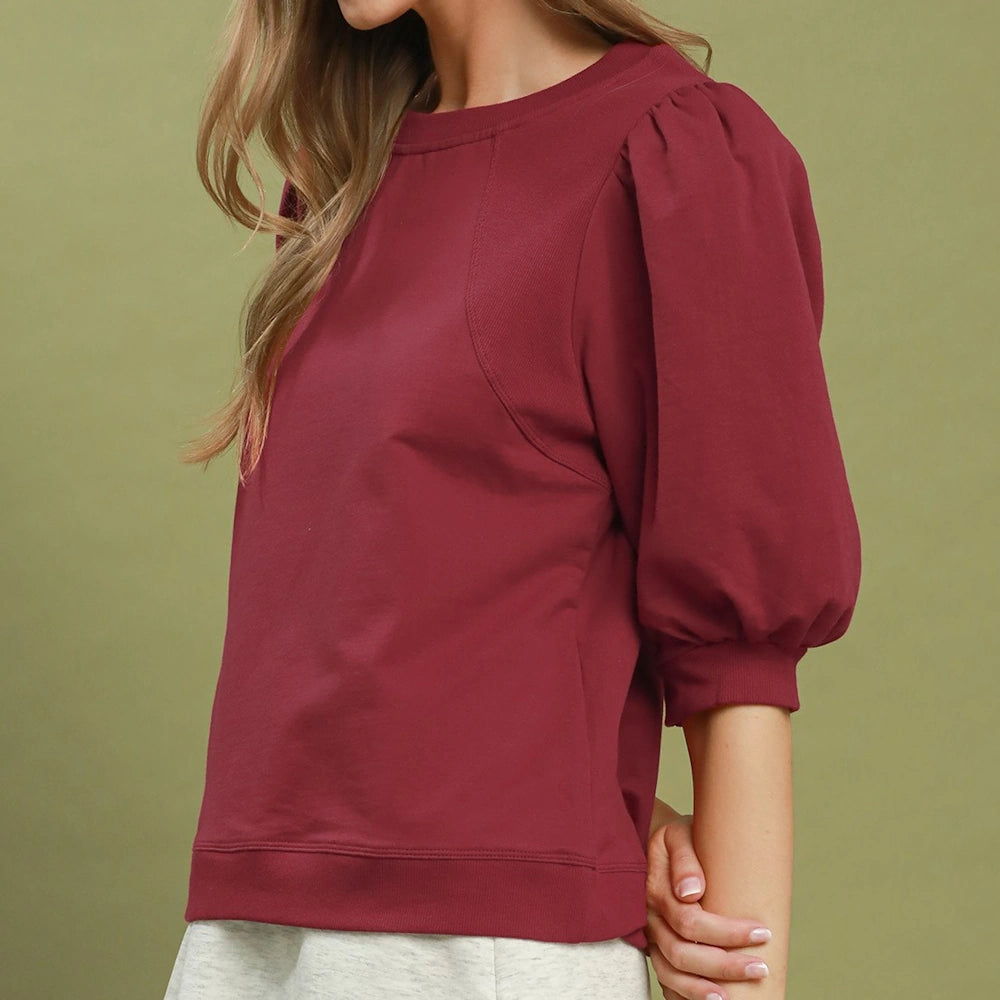 Woman wearing a wine red pullover sweatshirt top with three-quarter puffed sleeves, side profile view.