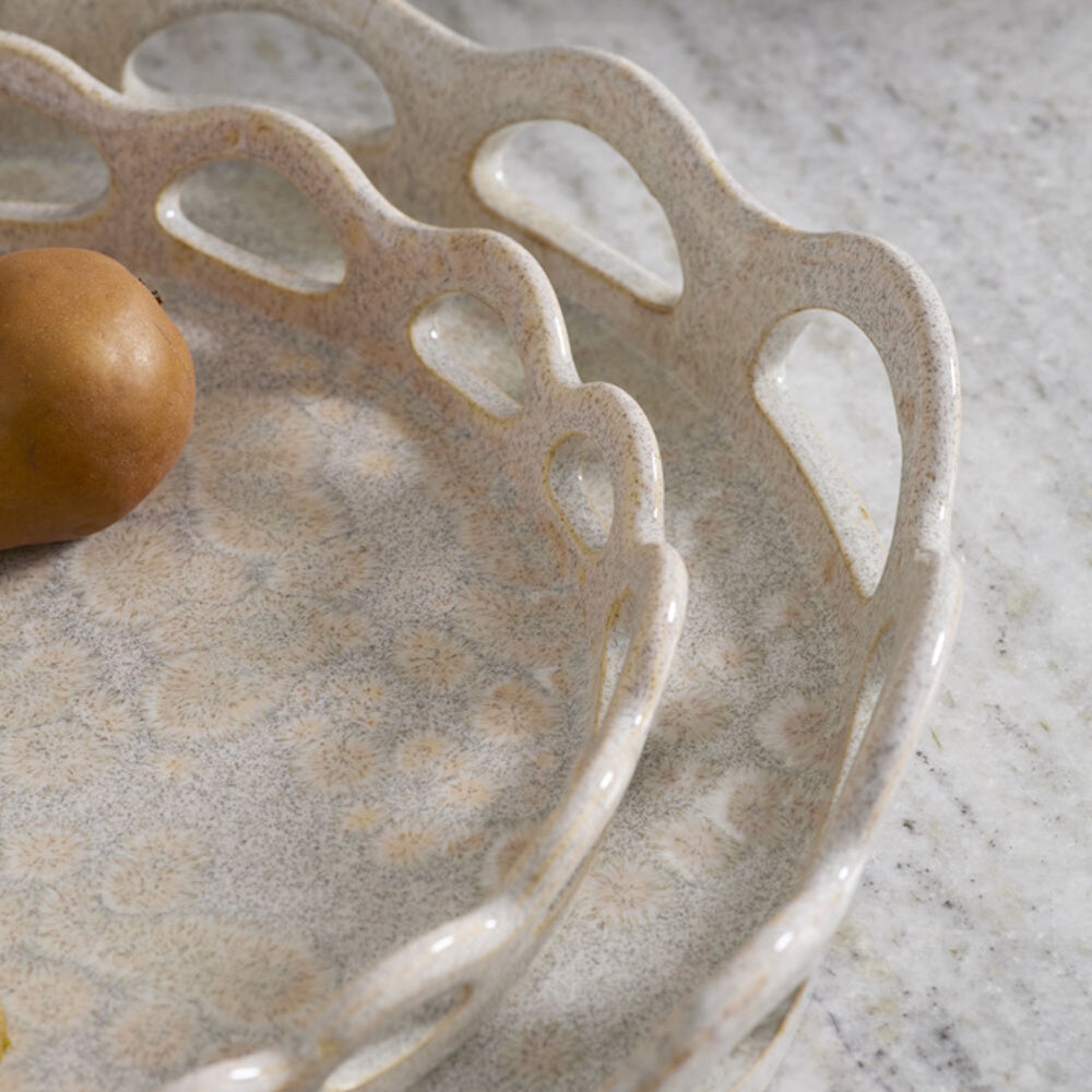 Close-up of two speckled ceramic trays with nested, scalloped cutout rims resting on marble.