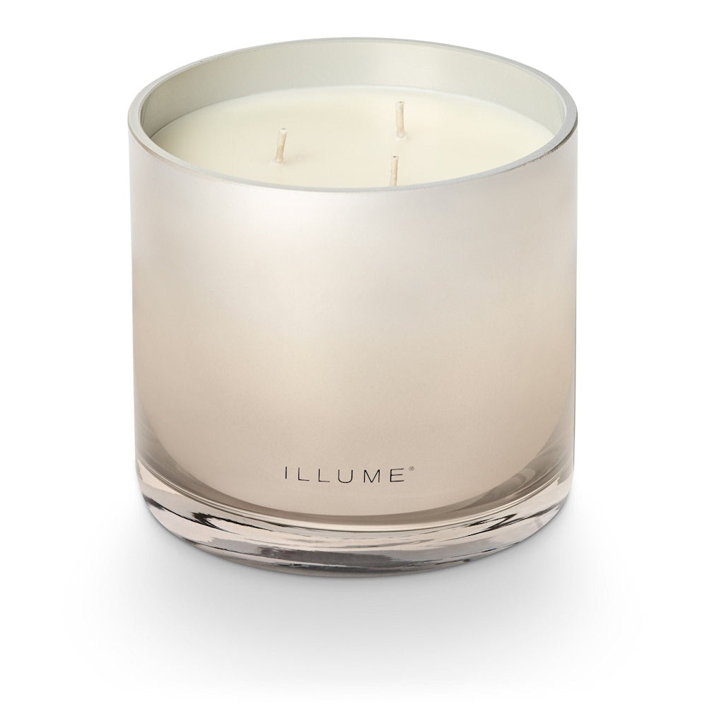 An unlit three-wick candle in a reflective glass jar with ILLUME branding.