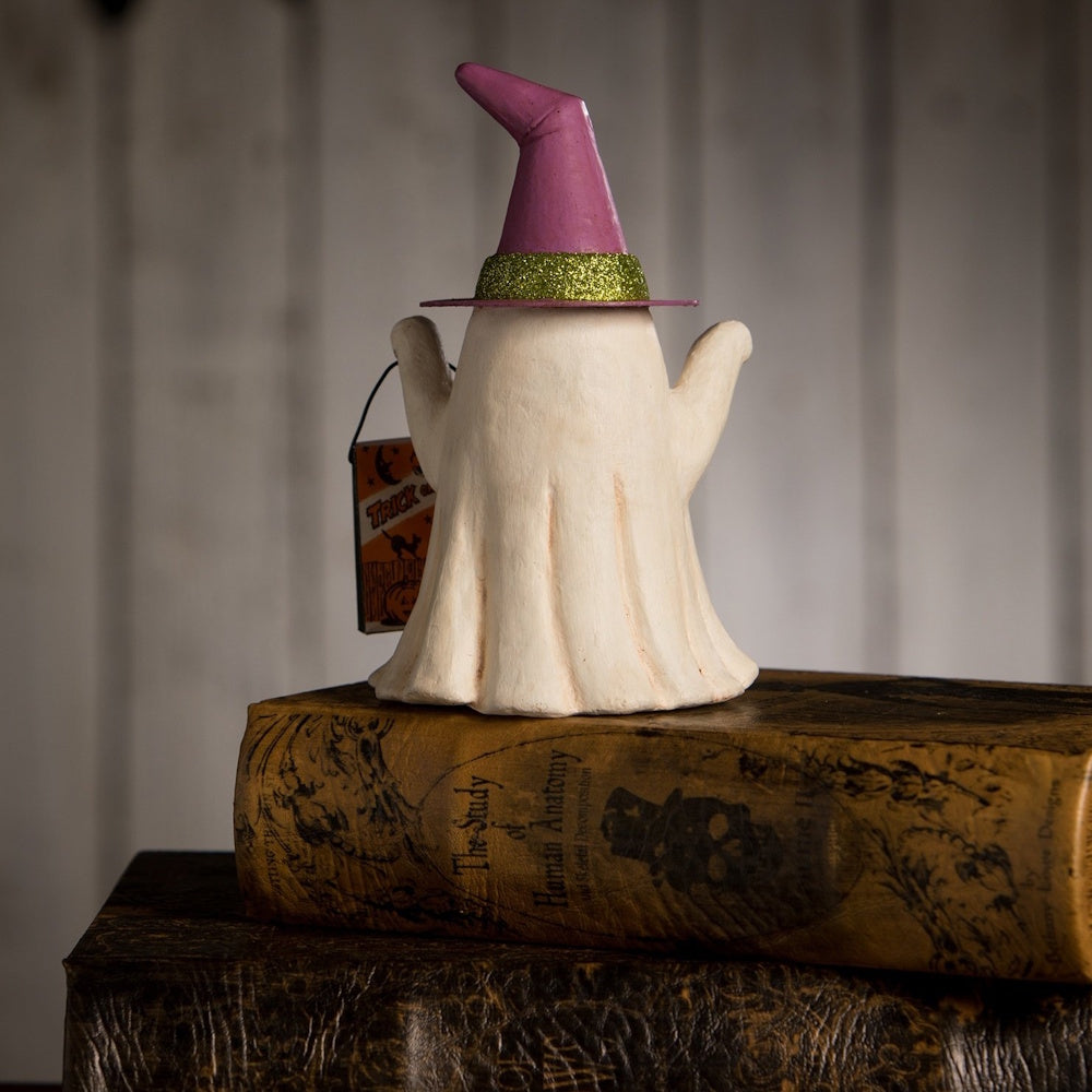 The back view of a figurine ghost wearing a purple witch hat, standing on stacked vintage-style books.