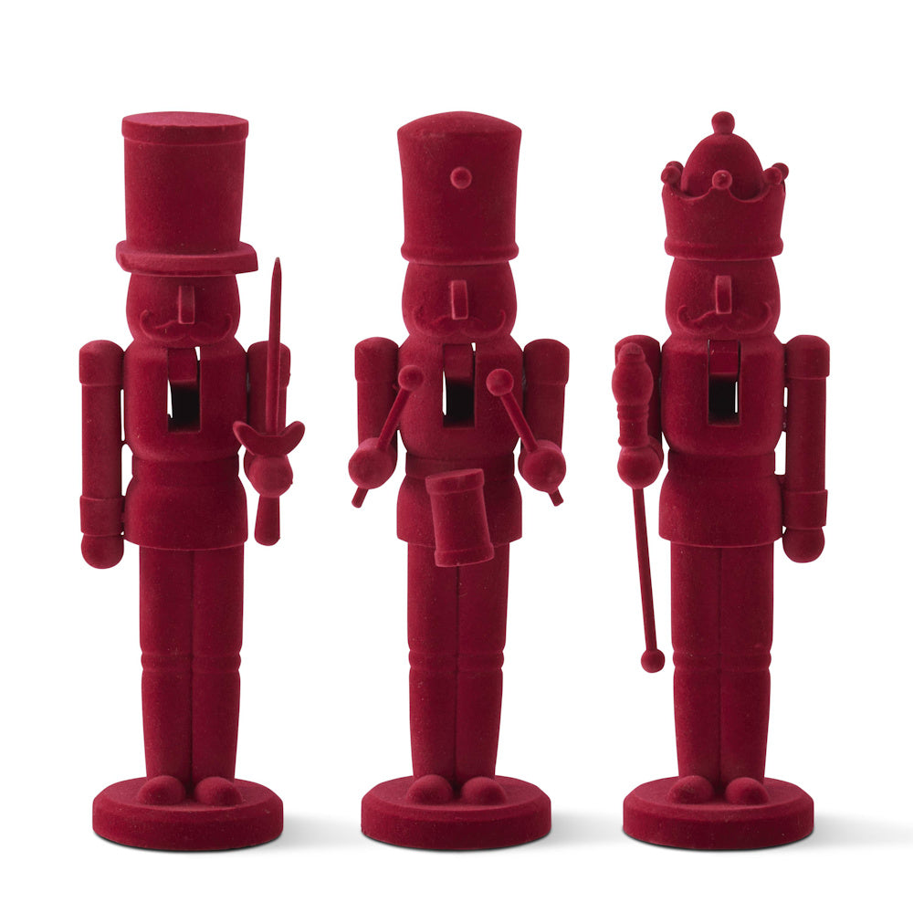 A set of three wooden nutcracker figures covered in a solid burgundy velvet texture.