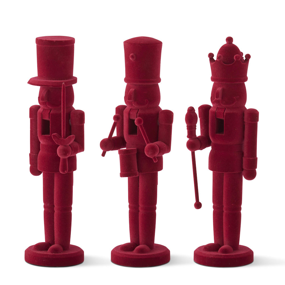 A set of three wooden nutcracker figures covered in a solid burgundy velvet texture.