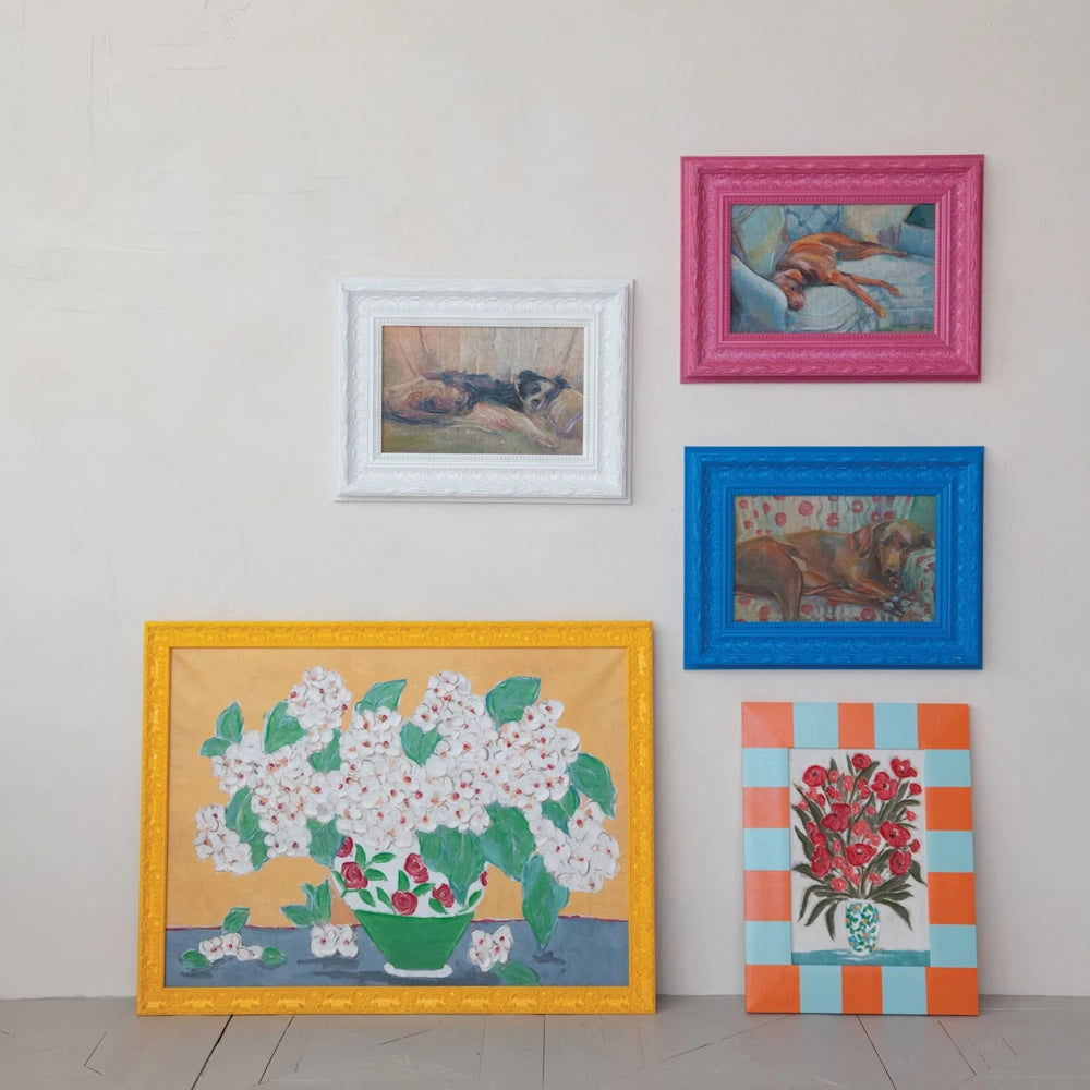 Gallery wall featuring colorful framed oil paintings of sleeping dogs and floral bouquets in vibrant antique-style frames.