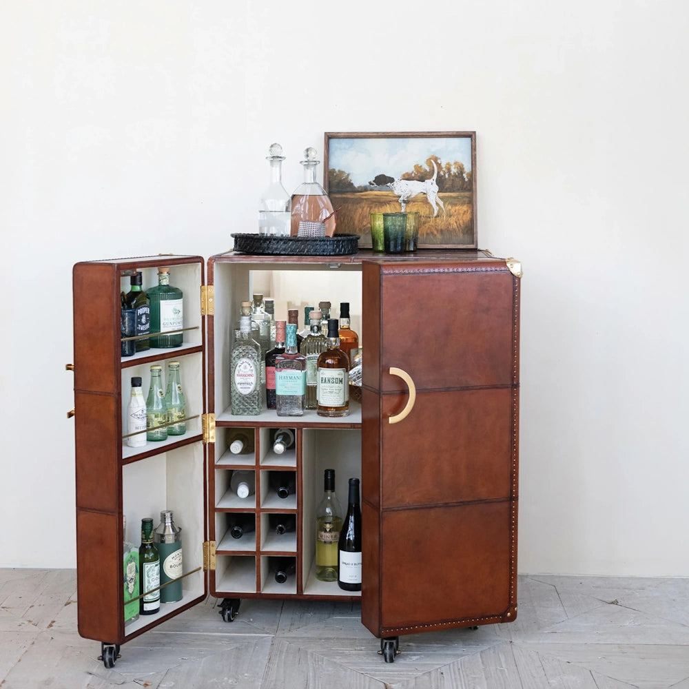 Framed pointer dog painting sitting on top of an open leather bar cabinet filled with liquor bottles.