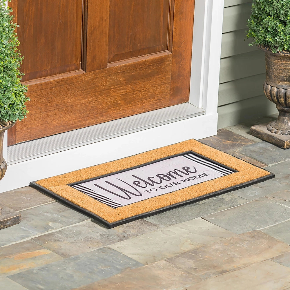 Welcome to our home decorative doormat with coir border on a stone porch in front of a wooden door.