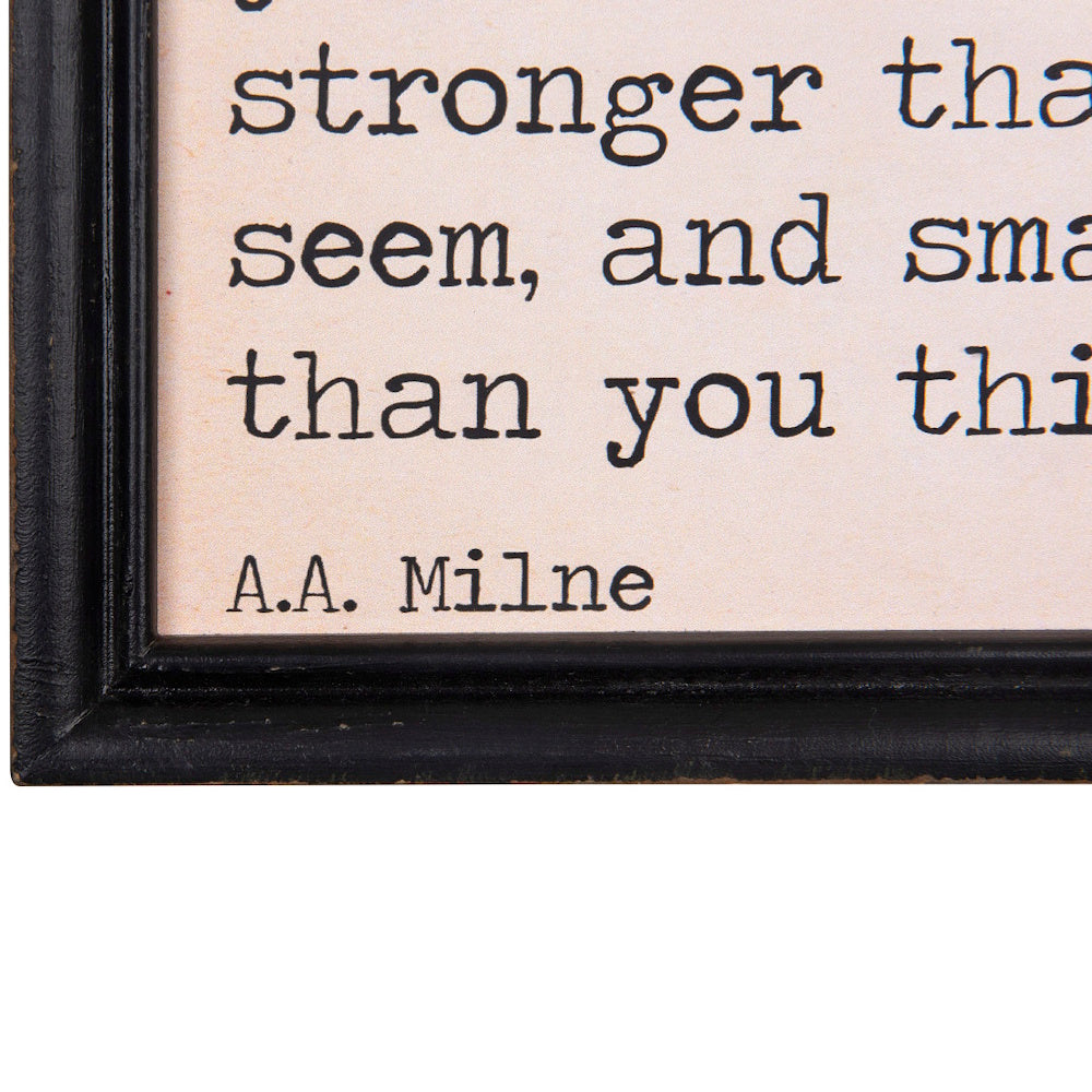 Close-up of a framed wood wall decor with an inspirational quote by A.A. Milne in typewriter font.