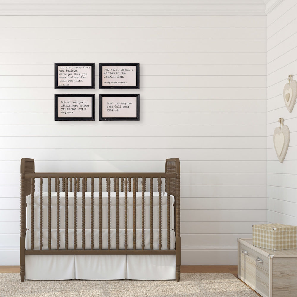 Four framed quote signs hanging above a brown wooden baby crib in a nursery with white shiplap walls.