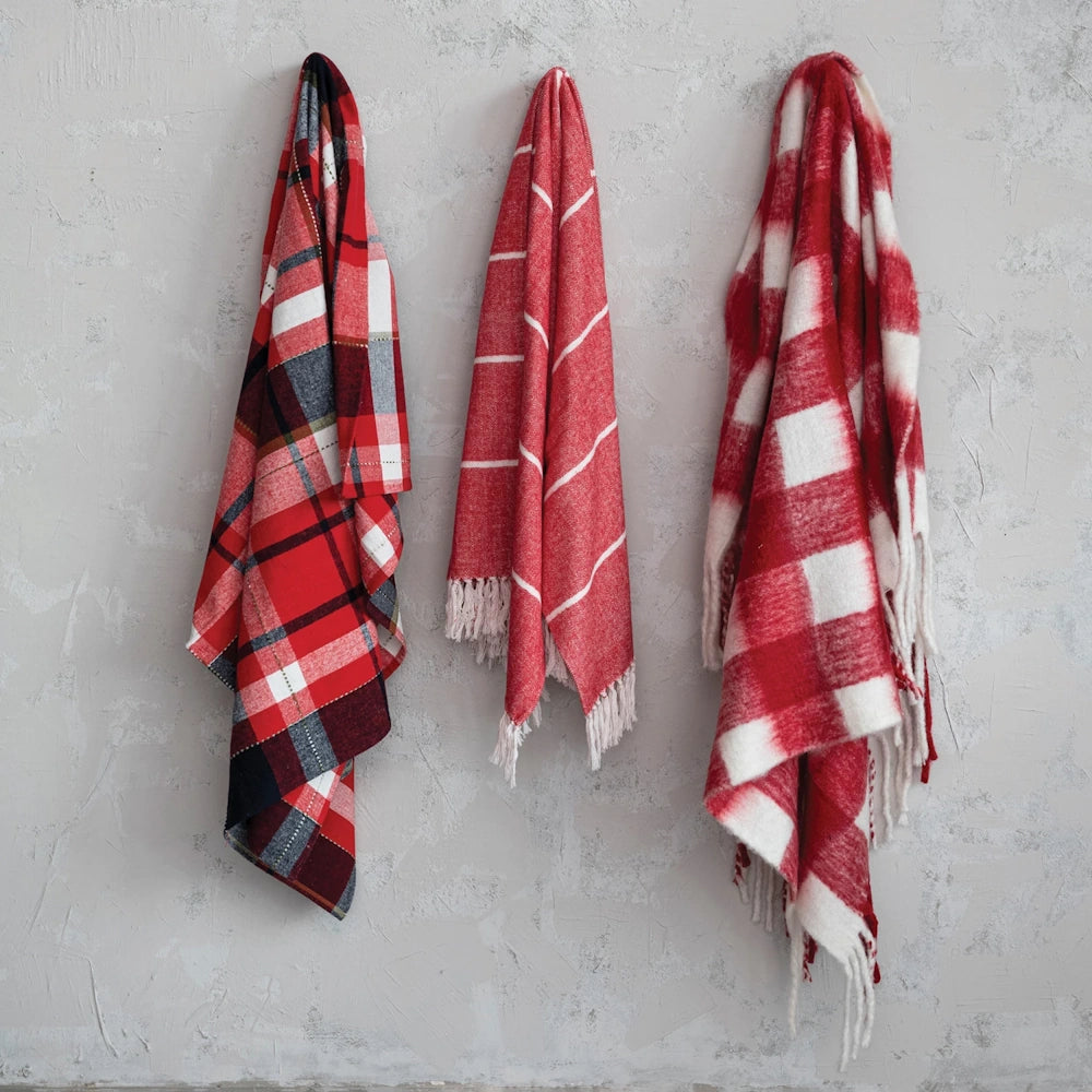 Three red patterned throw blankets hanging side-by-side against a light textured wall.