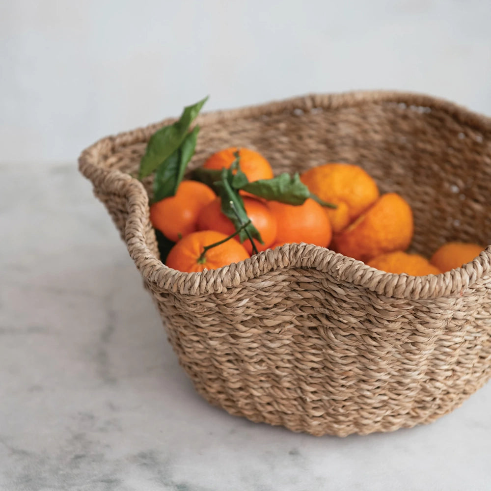Angled lifestyle view of a brown woven rattan ruffled bowl filled with fresh oranges.
