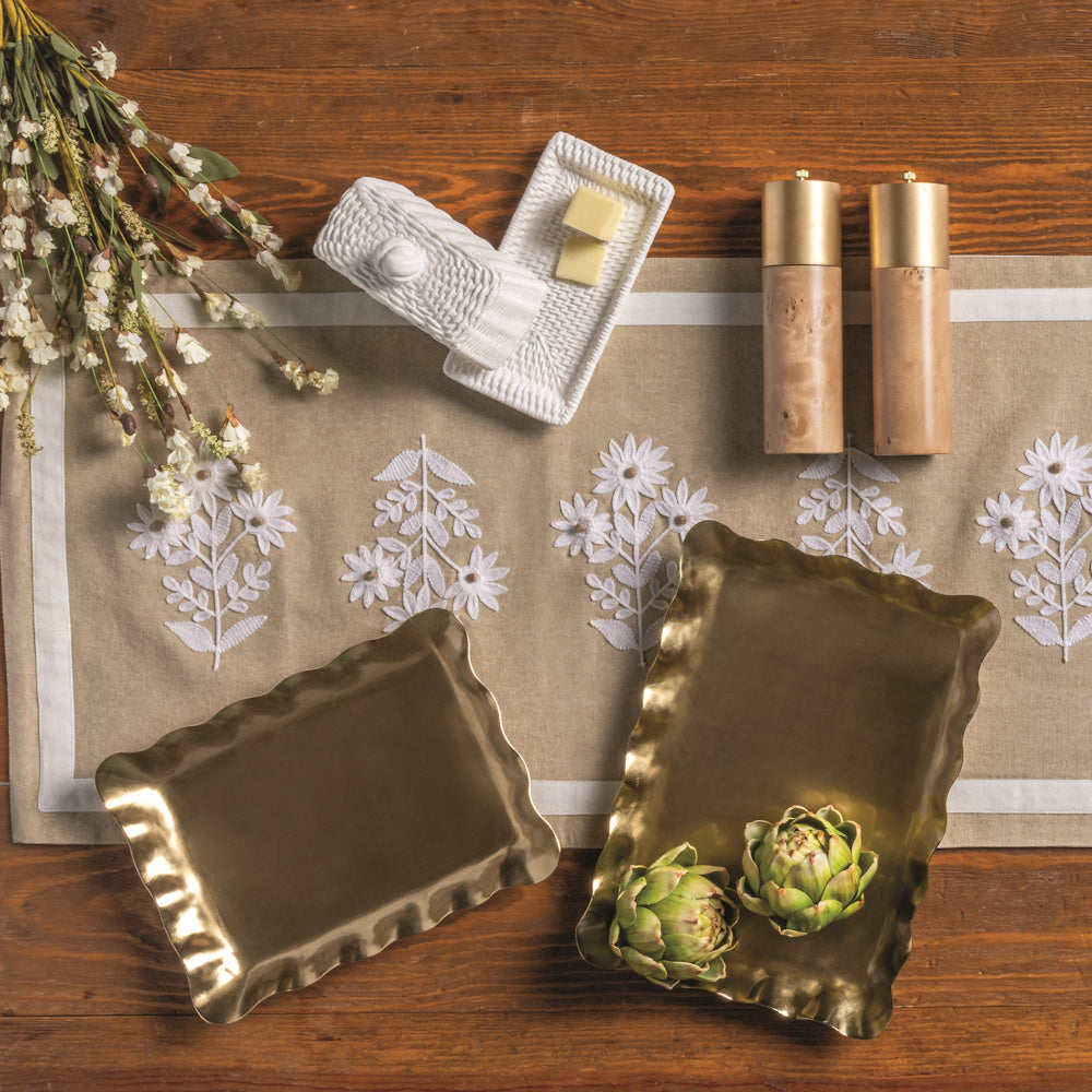 Flat lay of a woven white ceramic butter dish, gold ruffled trays, and wood salt and pepper shakers on a linen runner.