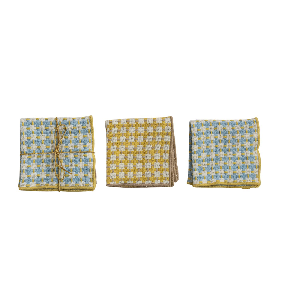 Three folded cotton dishcloths in blue and yellow woven grid patterns, one tied with twine on a white background.