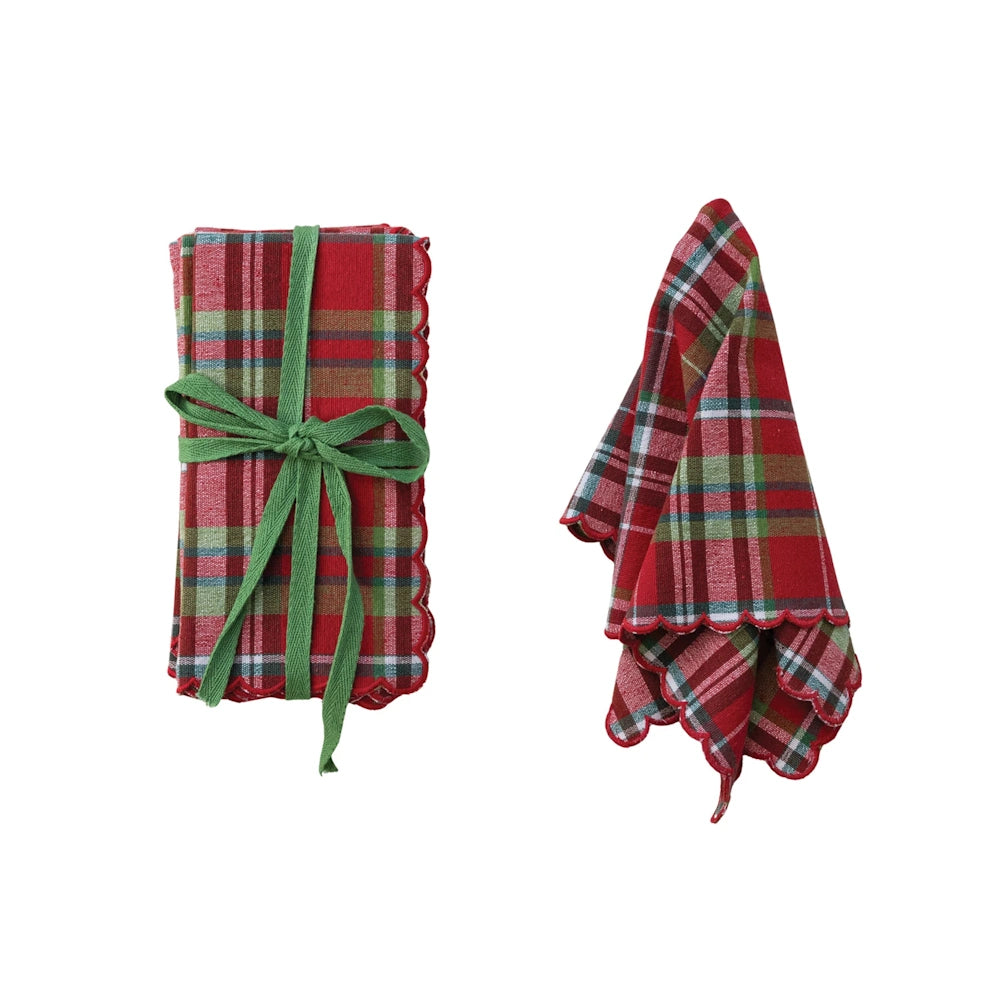 Red tartan plaid napkins with scalloped edges shown folded with a green bow and draped on a white background.