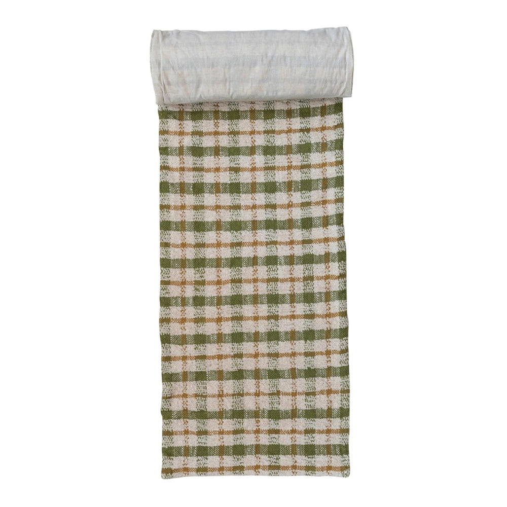 A woven cotton table runner with a green and brown plaid pattern, partially rolled up at the top.