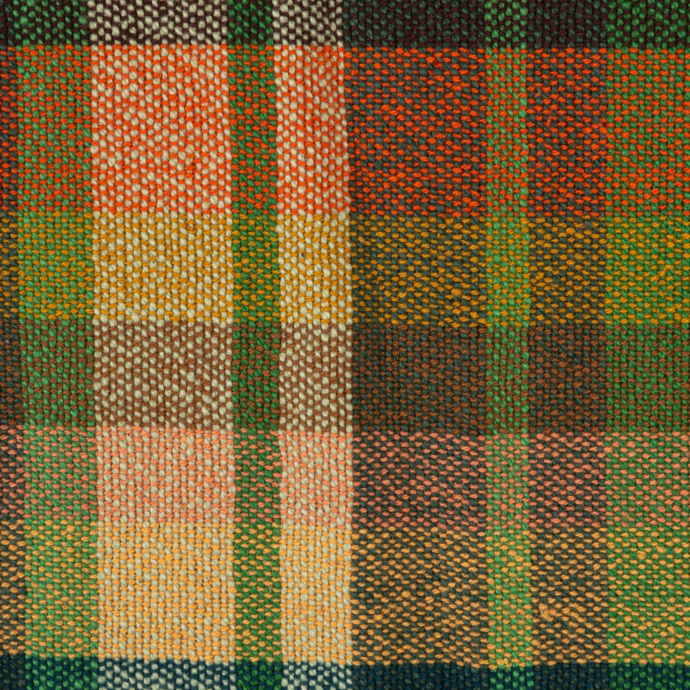 Close-up texture of a woven cotton plaid throw blanket featuring orange, green, and cream colors.