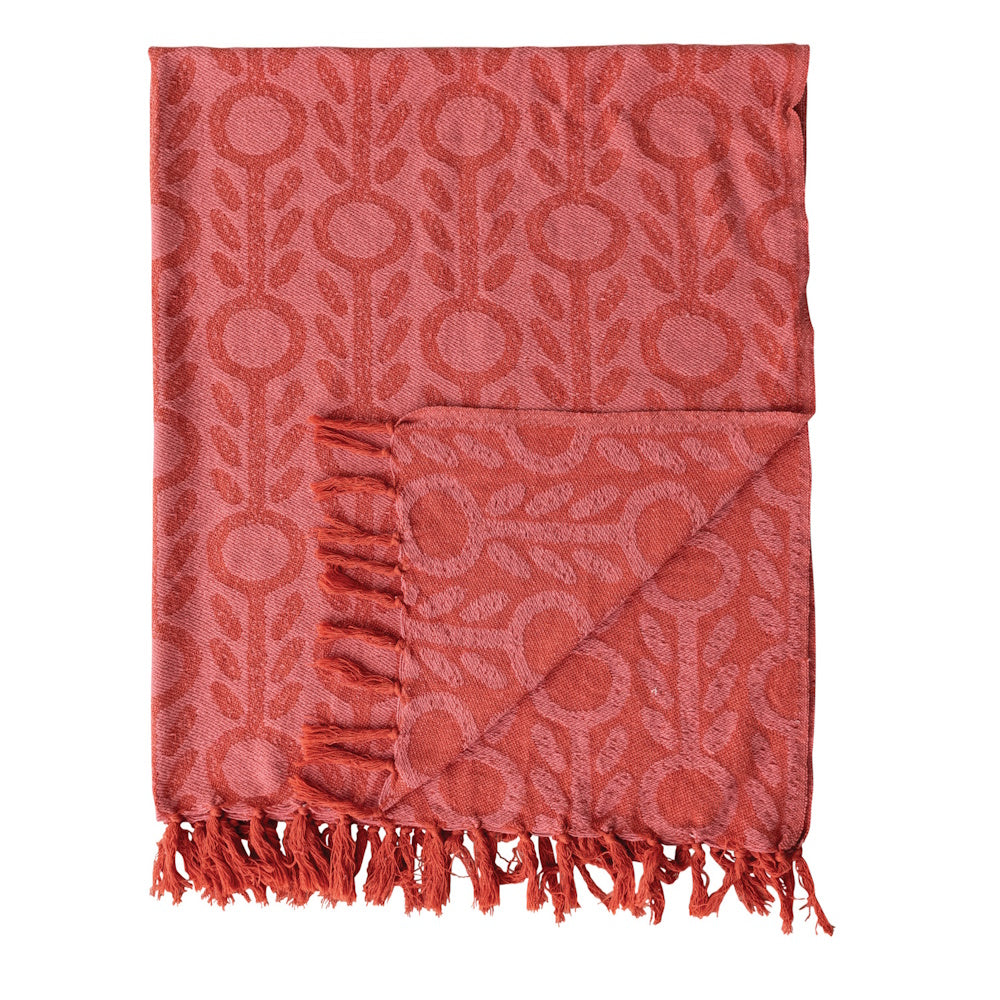 Folded woven recycled cotton blend jacquard throw in coral pink with a floral pattern and fringed edges.