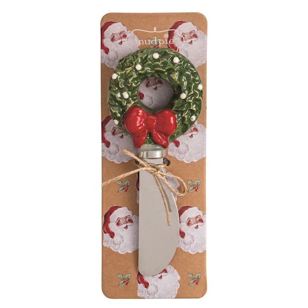 Cheese spreader with a ceramic Christmas wreath handle on a Santa-patterned backing card.