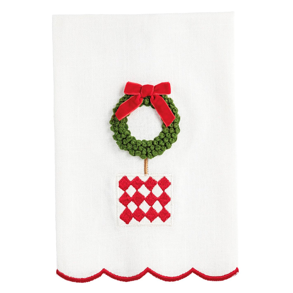 White towel with a green Christmas wreath tied with a red bow over a red and white pattern.