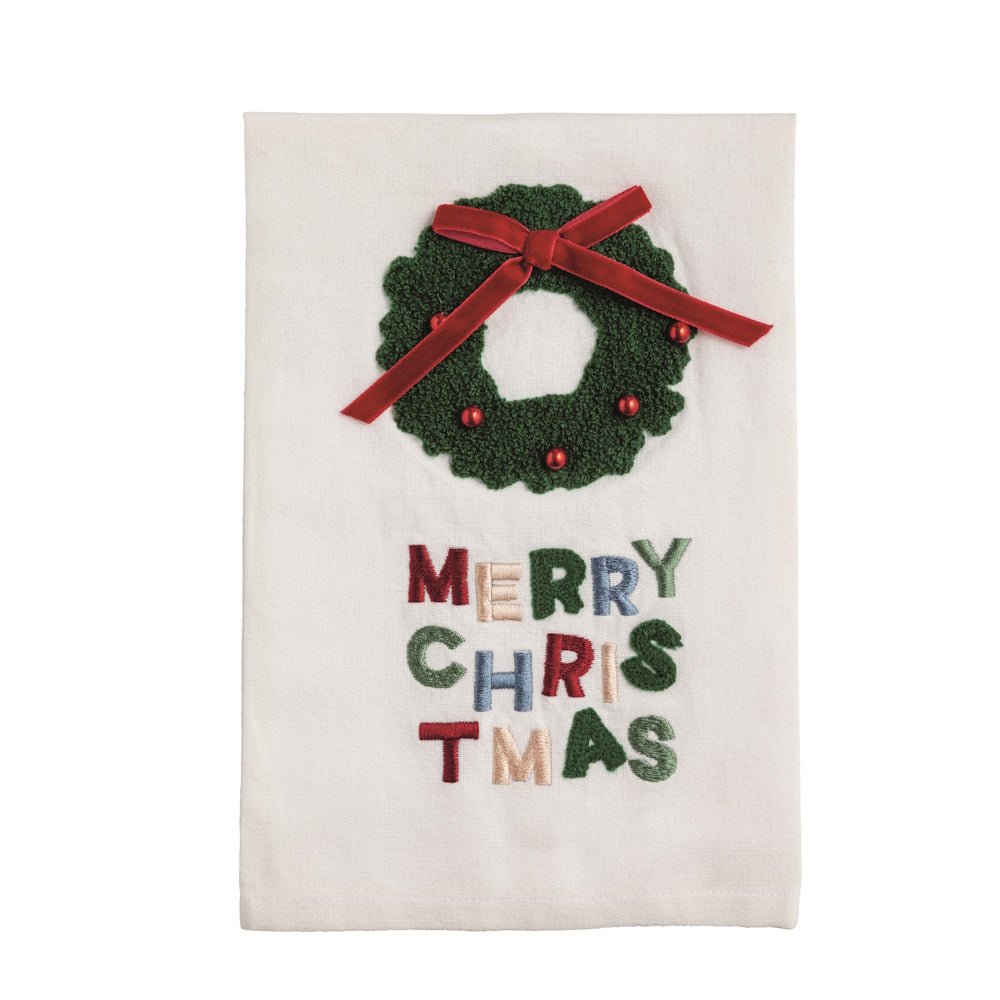 White Christmas kitchen towel featuring an embroidered green wreath with a red bow and multi-colored "Merry Christmas" text.