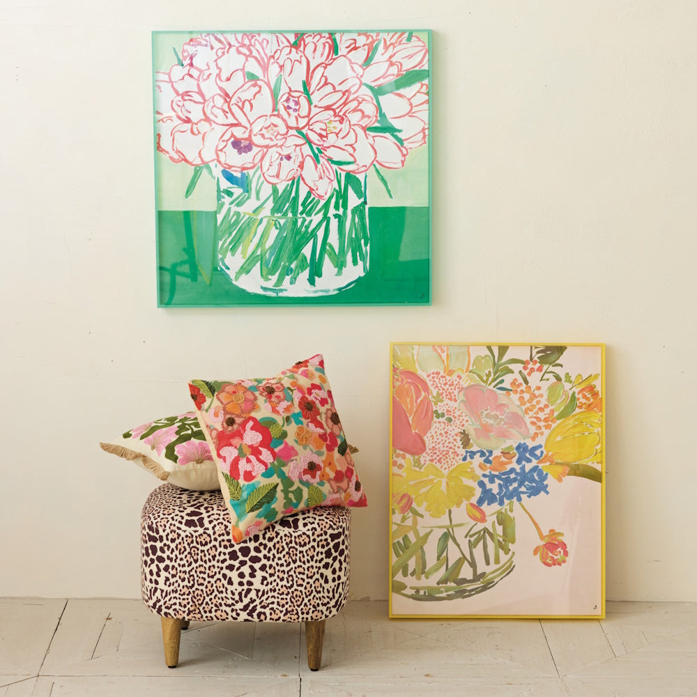 Hand-painted floral art in a yellow acrylic box frame, leaning near a leopard print ottoman with colorful pillows.