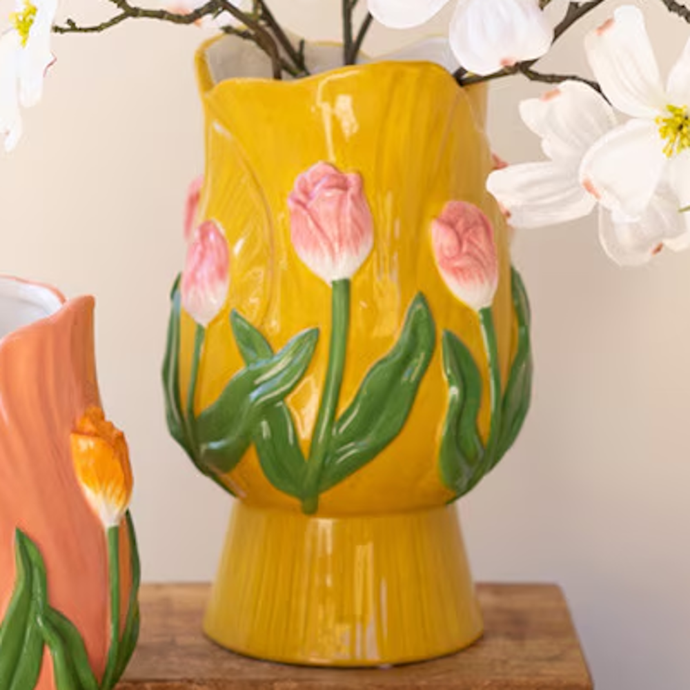 Yellow ceramic tulip-shaped vase with embossed pink tulips and green leaves on a wooden surface.