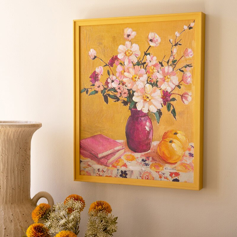 Yellow framed impressionist still life painting of pink flowers in a purple vase with books and fruit on a yellow background.