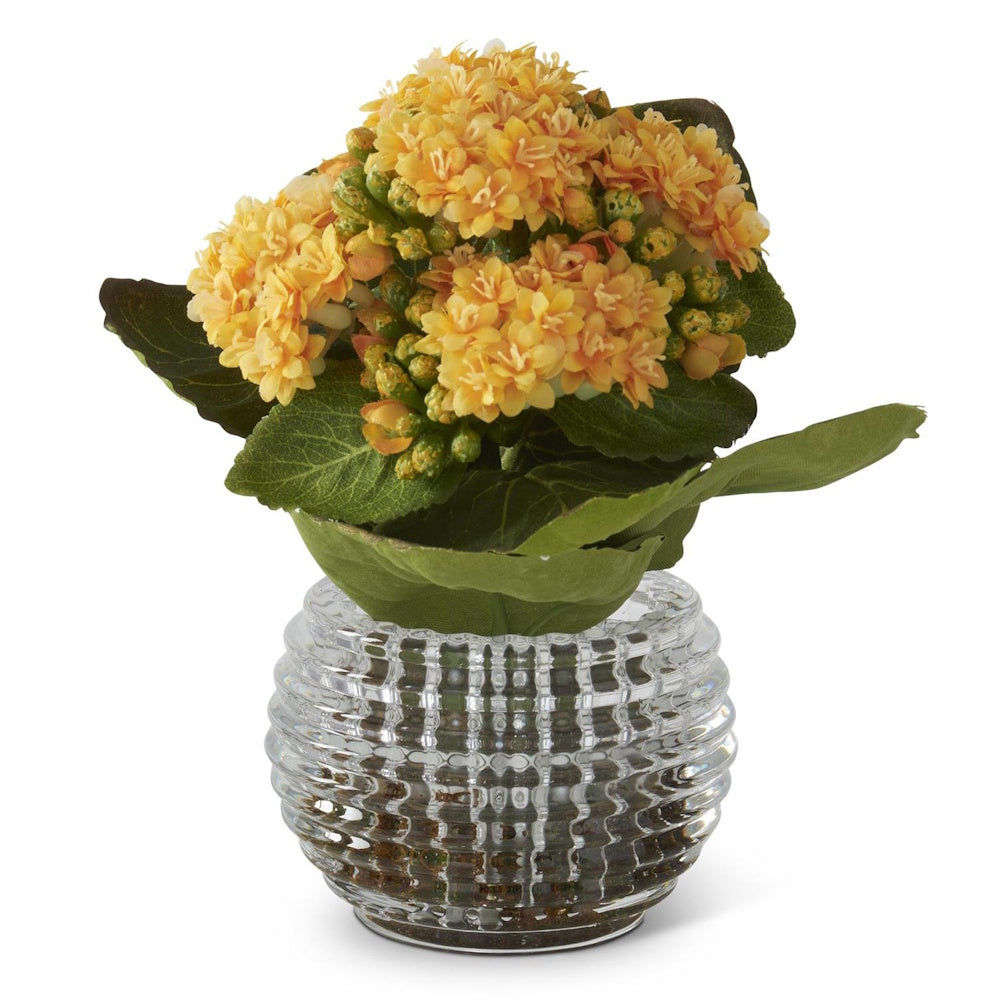 Artificial yellow Kalanchoe flowers with green leaves in a ribbed clear glass vase.