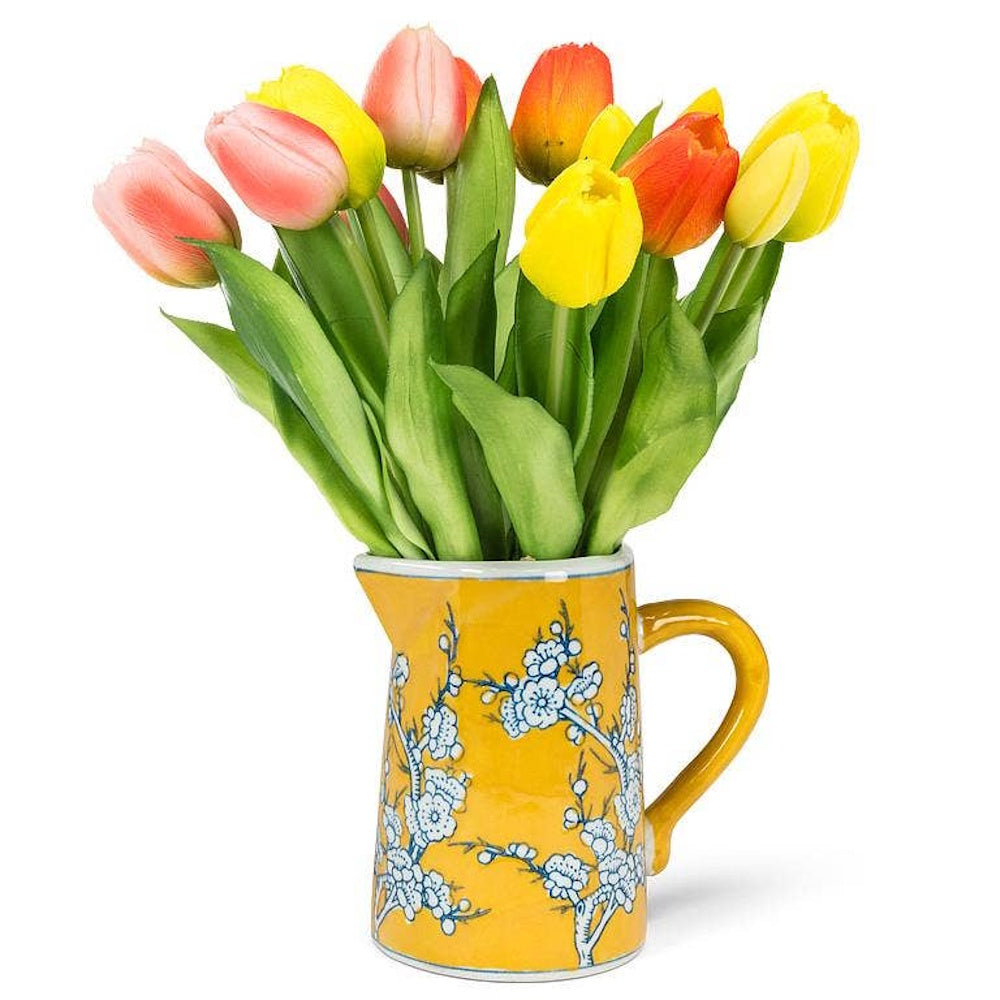 Colorful tulips in a small yellow ceramic pitcher with a blue and white cherry blossom floral design.