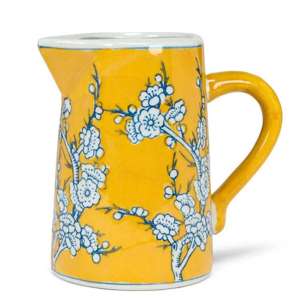 Small yellow ceramic jug with white and blue floral cherry blossom pattern on a white background.