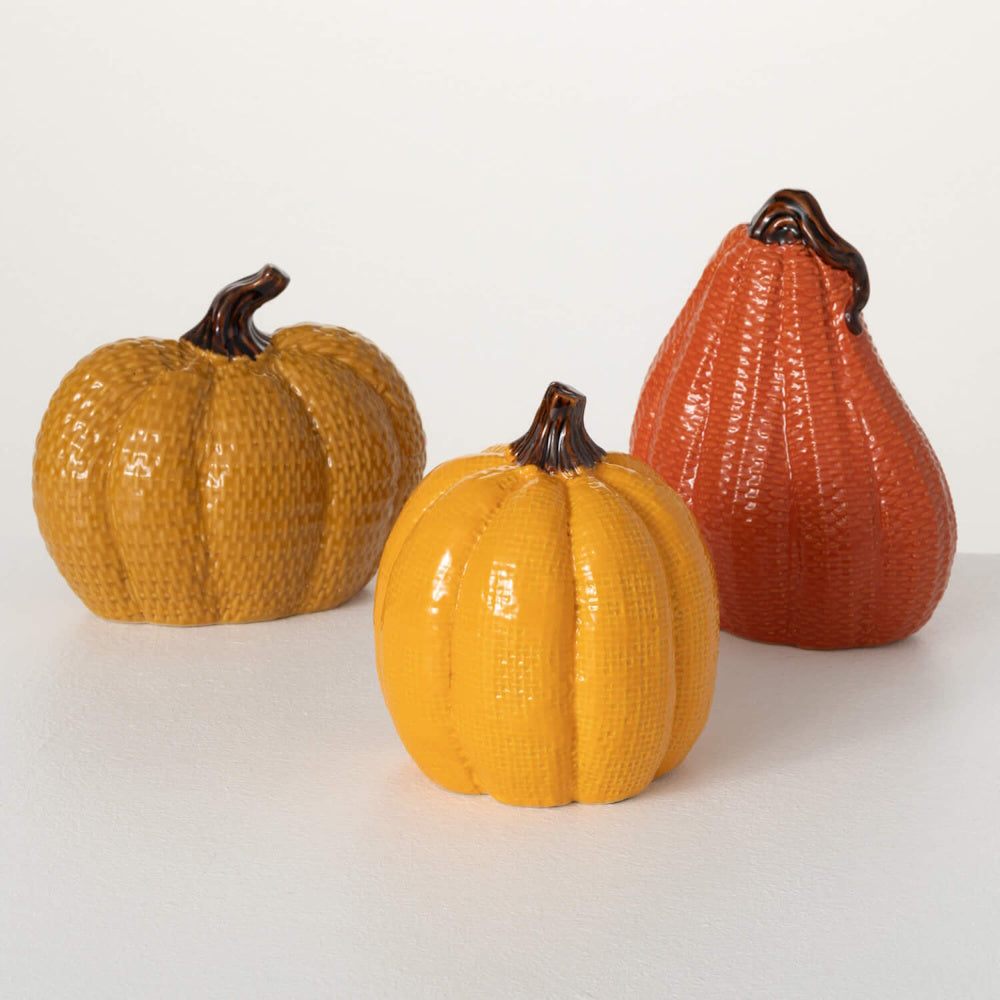 Three glossy, textured decorative ceramic pumpkins in mustard yellow, bright yellow, and orange.