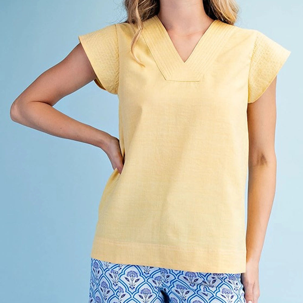 Woman wearing a yellow V-neck blouse with trapunto stitching and cap sleeves, paired with blue patterned pants.