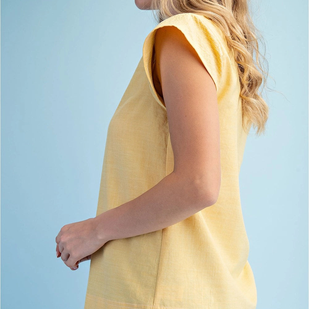 Side view of a woman wearing a yellow trapunto stitched V-neck blouse with loose cap sleeves against a light blue background.