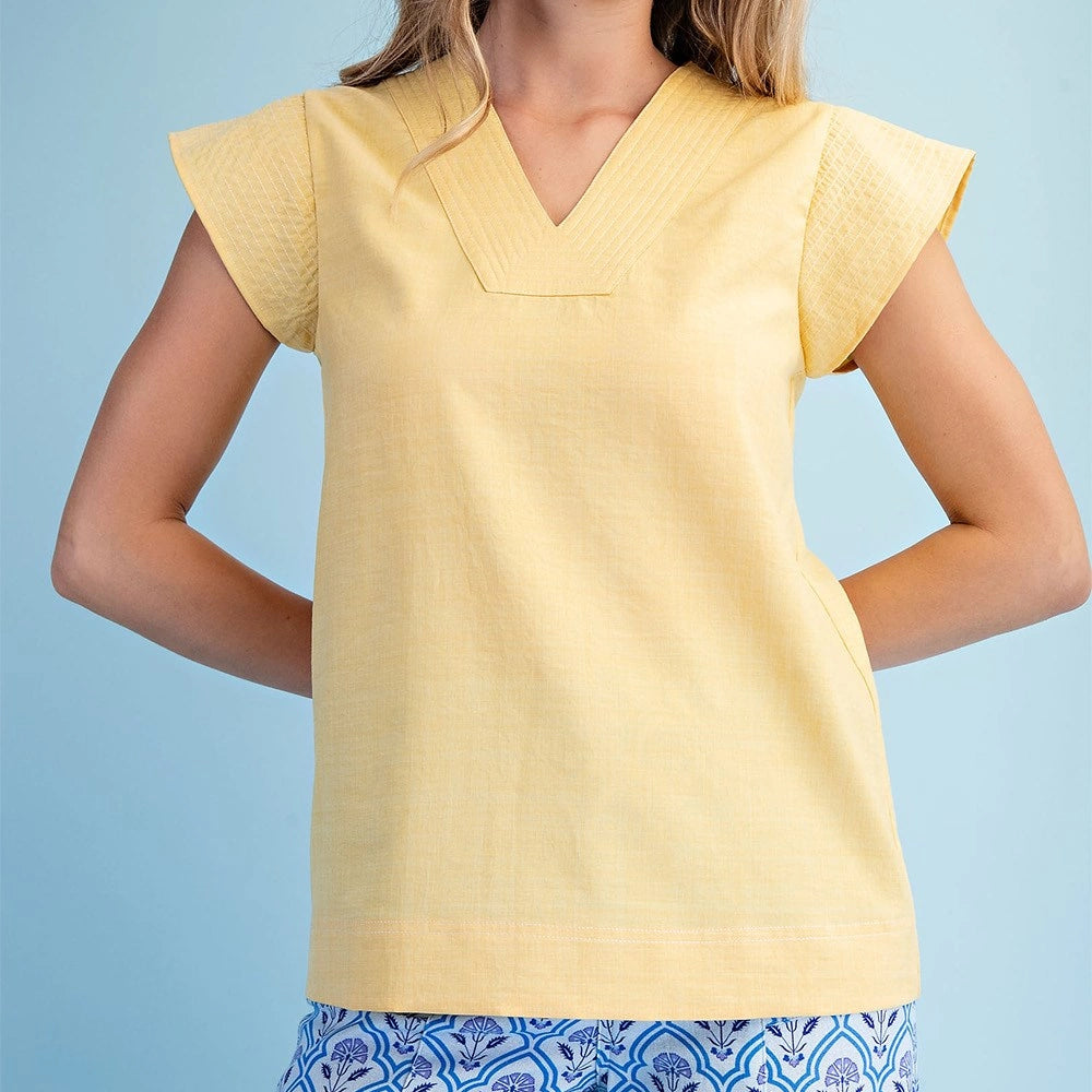 A woman wearing a pale yellow V-neck blouse with trapunto stitching on the neckline and loose cap sleeves.