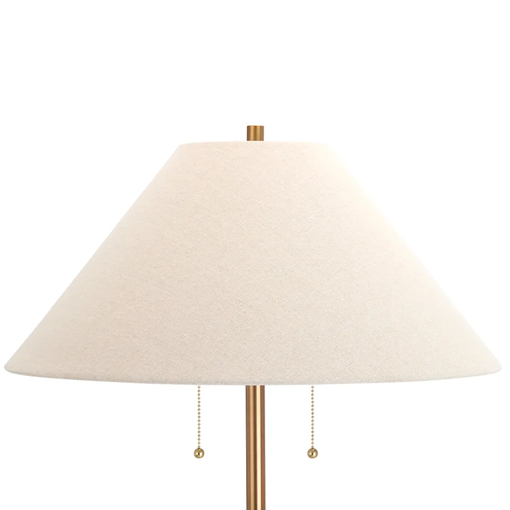 Close-up of a lamp with a cream linen shade, a brass pole, and dual pull-chain switches.