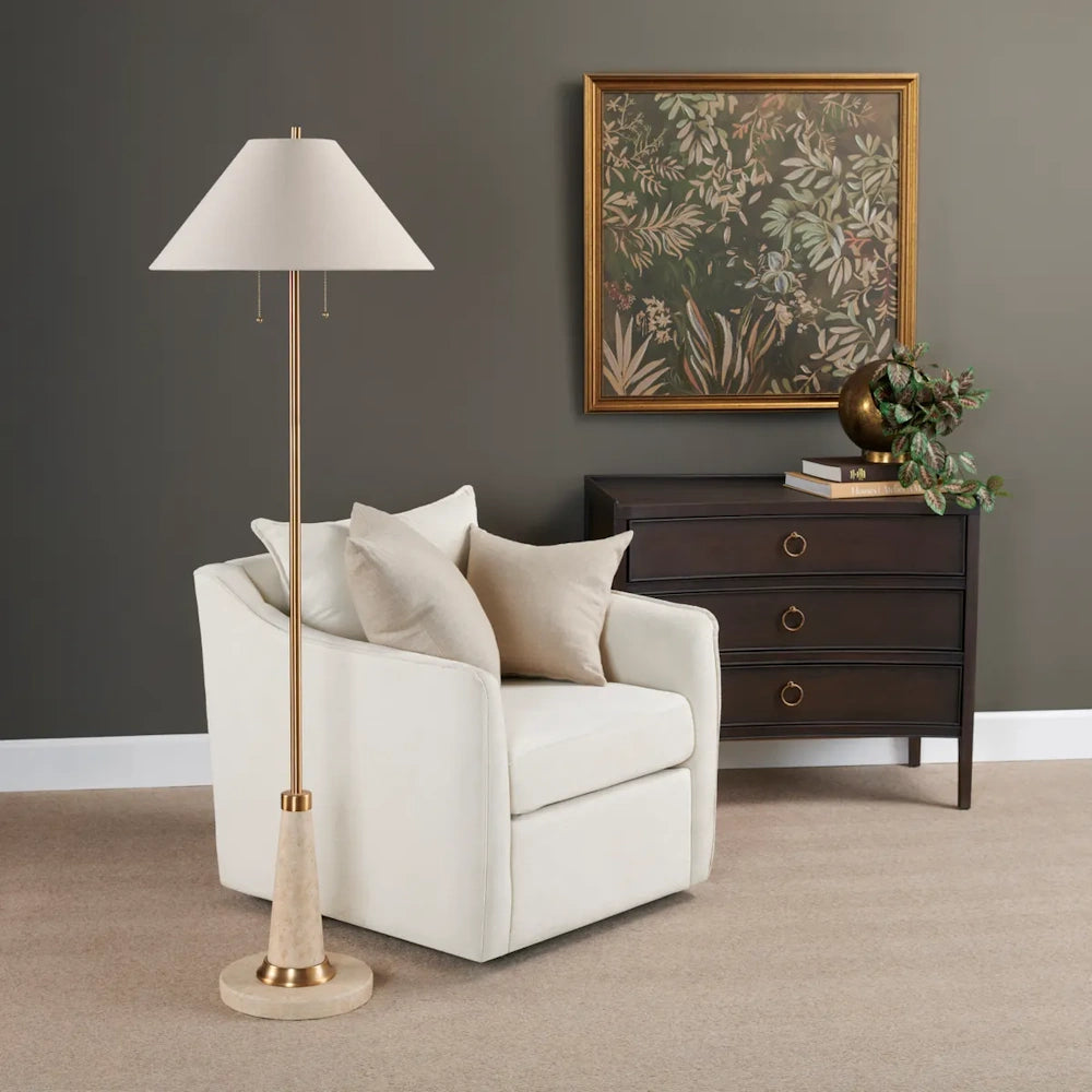 Tall brass floor lamp next to a white armchair in a stylish room with dark furniture and framed art.