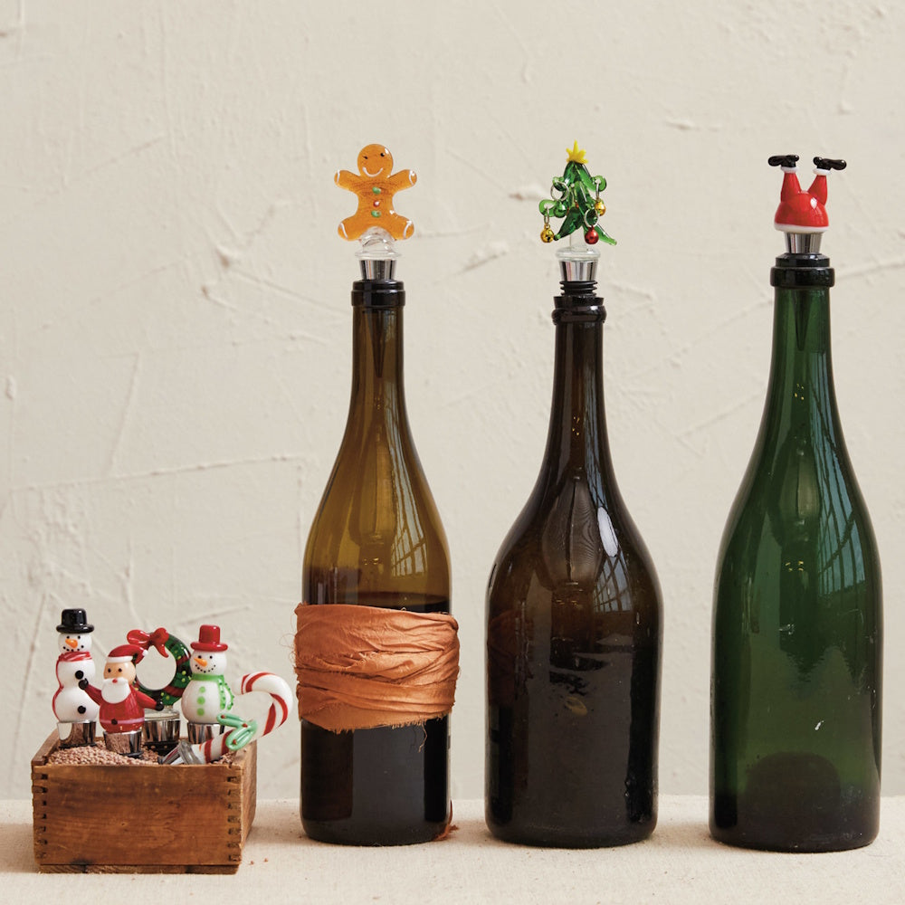 Christmas-themed bottle stoppers with a gingerbread man, tree, and upside-down Santa on glass bottles.